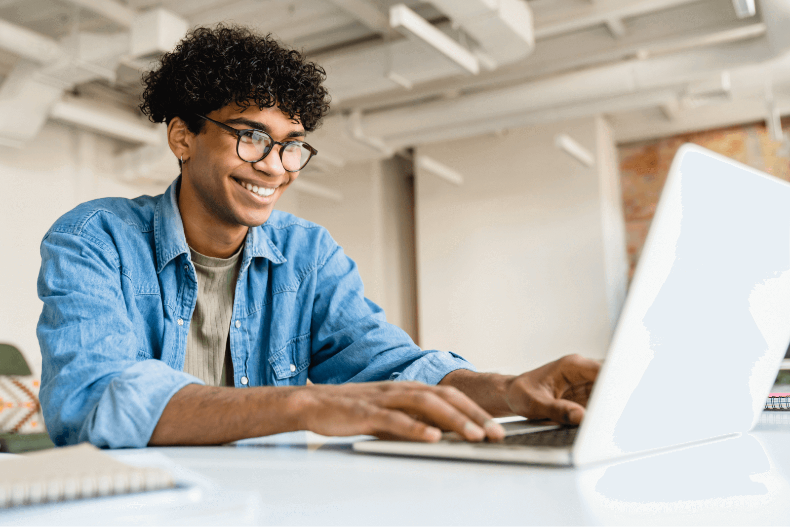 Jovem com óculos sorri enquanto trabalha em seu laptop, refletindo a inovação na administração de prédios e melhorias.
